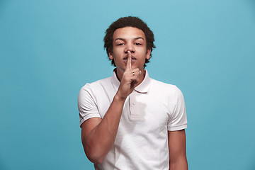 Image showing The young man whispering a secret behind her hand over blue background