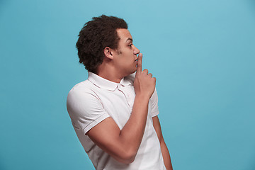 Image showing The young man whispering a secret behind her hand over blue background