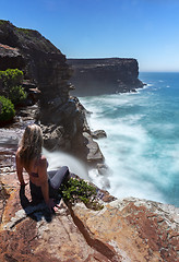 Image showing Woman watches waterfall flows off cliffs into ocean