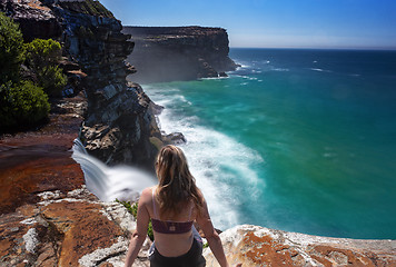 Image showing Female on edge watching waterfalls flow into the ocean