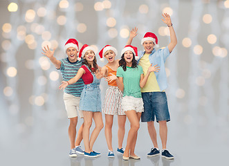 Image showing happy friends in santa hats over festive lights