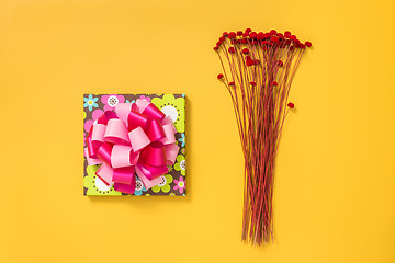 Image showing Bright gift box and red flowers on yellow background