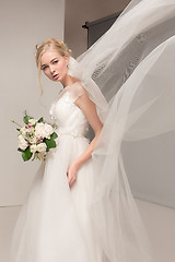 Image showing Bride in beautiful dress standing indoors in white studio interior like at home. Trendy wedding style shot. Young attractive caucasian model like a bride tender looking.