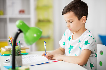 Image showing boy with book writing to notebook at home