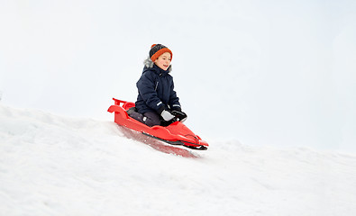 Image showing happy boy sliding on sled down snow hill in winter