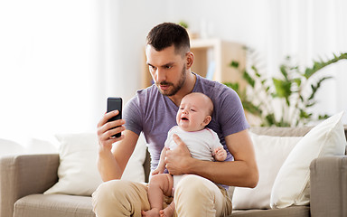 Image showing father with crying baby and smartphone at home