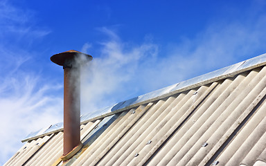 Image showing Smoke From The Chimney On The Old Roof Against The Blue Sky 