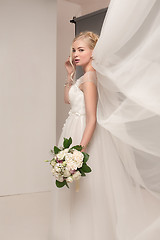 Image showing Bride in beautiful dress standing indoors in white studio interior like at home. Trendy wedding style shot. Young attractive caucasian model like a bride tender looking.