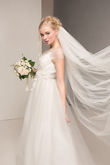 Image showing Bride in beautiful dress standing indoors in white studio interior like at home. Trendy wedding style shot. Young attractive caucasian model like a bride tender looking.