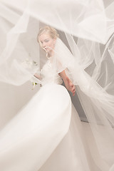 Image showing Bride in beautiful dress standing indoors in white studio interior like at home. Trendy wedding style shot. Young attractive caucasian model like a bride tender looking.