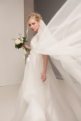 Image showing Bride in beautiful dress standing indoors in white studio interior like at home. Trendy wedding style shot. Young attractive caucasian model like a bride tender looking.