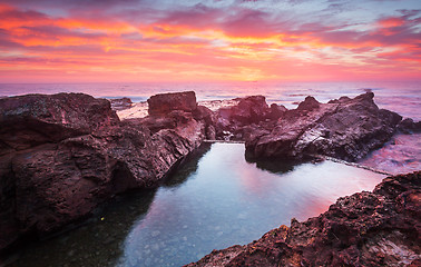 Image showing Blazing red sunrise over rock pool