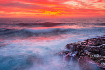 Image showing Res skies over ocean as waves surge over rocks