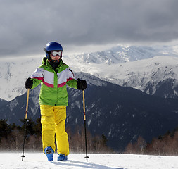Image showing Young skier with ski poles in sun mountains and gray sky before 