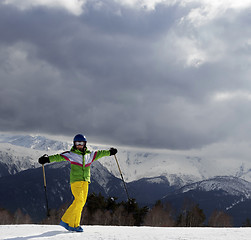 Image showing Happy young skier with ski poles in sun mountains and cloudy gra