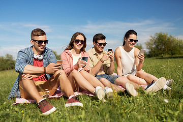 Image showing smiling friends with smartphones sitting on grass