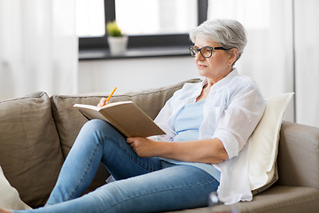 Image showing senior woman writing to notebook or diary at home