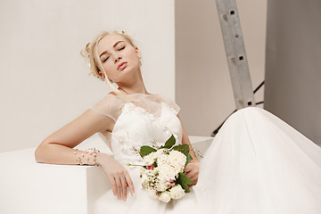 Image showing Bride in beautiful dress standing indoors in white studio interior like at home. Trendy wedding style shot. Young attractive caucasian model like a bride tender looking.