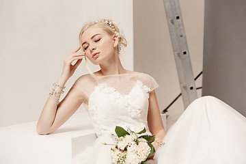 Image showing Bride in beautiful dress standing indoors in white studio interior like at home. Trendy wedding style shot. Young attractive caucasian model like a bride tender looking.