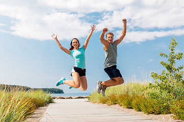 Image showing happy couple in sports clothes jumping on beach