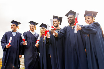 Image showing happy students in mortar boards with diplomas