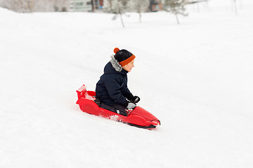 Image showing happy boy sliding on sled down snow hill in winter