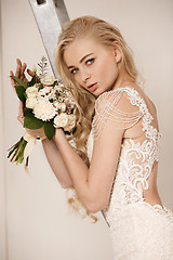 Image showing Bride in beautiful dress standing indoors in white studio interior like at home. Trendy wedding style shot. Young attractive caucasian model like a bride tender looking.