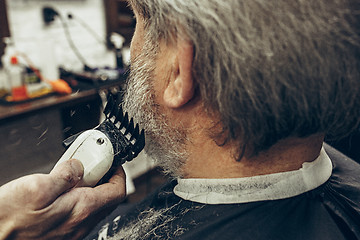 Image showing Close-up side back view handsome senior bearded caucasian man getting beard grooming in modern barbershop.