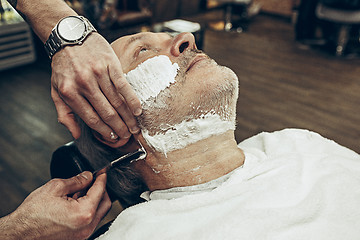 Image showing Close-up side top view handsome senior bearded caucasian man getting beard grooming in modern barbershop.