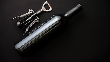 Image showing Red wine bottle and corkscrew on black matte background.