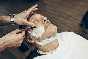 Image showing Close-up side top view handsome senior bearded caucasian man getting beard grooming in modern barbershop.