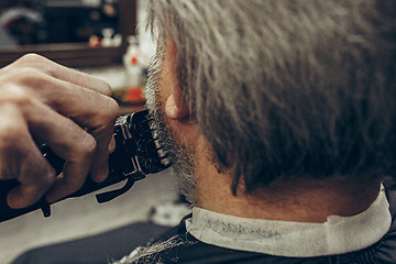 Image showing Close-up side back view handsome senior bearded caucasian man getting beard grooming in modern barbershop.
