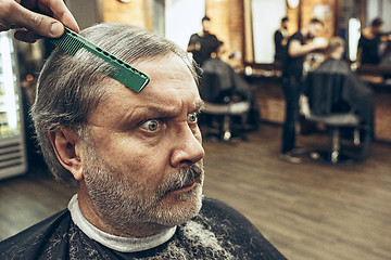 Image showing The hands of barber making haircut attractive old man in barbershop