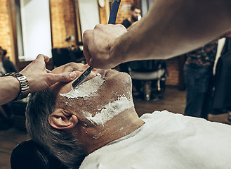 Image showing Close-up side top view handsome senior bearded caucasian man getting beard grooming in modern barbershop.