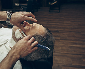 Image showing Close-up side top view handsome senior bearded caucasian man getting beard grooming in modern barbershop.