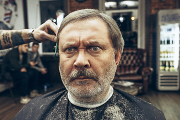 Image showing The hands of barber making haircut attractive old man in barbershop