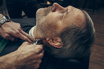 Image showing Close-up side back view handsome senior bearded caucasian man getting beard grooming in modern barbershop.