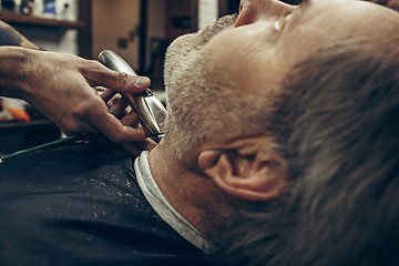 Image showing Close-up side back view handsome senior bearded caucasian man getting beard grooming in modern barbershop.