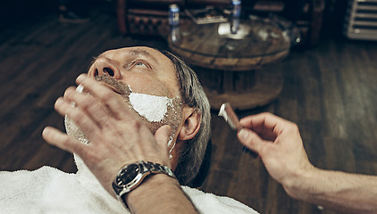 Image showing Close-up side top view handsome senior bearded caucasian man getting beard grooming in modern barbershop.