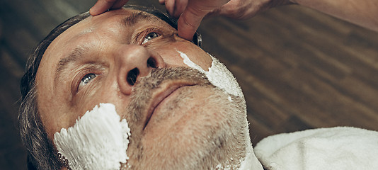 Image showing Close-up side top view handsome senior bearded caucasian man getting beard grooming in modern barbershop.