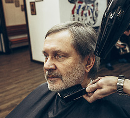 Image showing Close-up side view portrait of handsome senior bearded caucasian man getting beard grooming in modern barbershop.