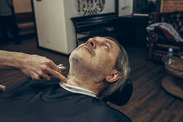 Image showing Close-up side profile view portrait of handsome senior bearded caucasian man getting beard grooming in modern barbershop.