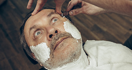 Image showing Close-up side top view handsome senior bearded caucasian man getting beard grooming in modern barbershop.