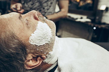 Image showing Close-up side view portrait of handsome senior bearded caucasian man getting beard grooming in modern barbershop.