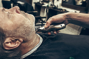 Image showing Close-up side profile view portrait of handsome senior bearded caucasian man getting beard grooming in modern barbershop.