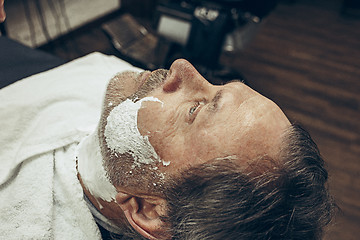 Image showing Close-up side top view handsome senior bearded caucasian man getting beard grooming in modern barbershop.