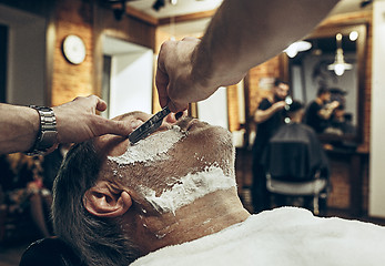 Image showing Close-up side top view handsome senior bearded caucasian man getting beard grooming in modern barbershop.