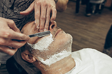 Image showing Close-up side top view handsome senior bearded caucasian man getting beard grooming in modern barbershop.