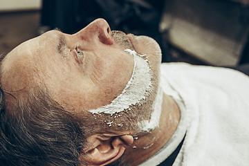 Image showing Close-up side top view handsome senior bearded caucasian man getting beard grooming in modern barbershop.