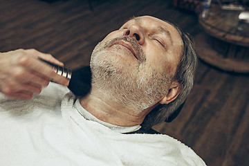 Image showing Close-up side top view handsome senior bearded caucasian man getting beard grooming in modern barbershop.